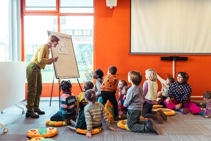 een Leesjury-begeleidster toont een groep kinderen iets op een flip-over